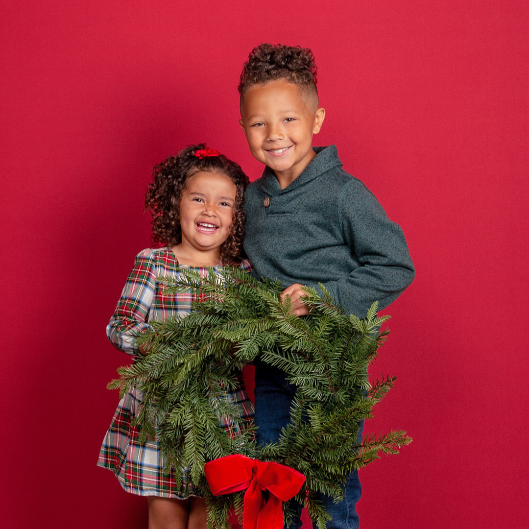 Siblings holding a wreath posing for holiday photos