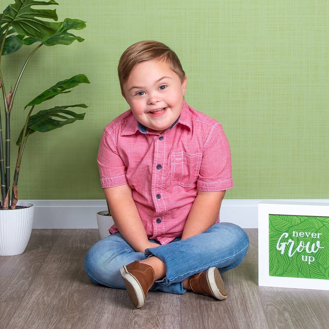 Boy sitting on floor with plant prop on a green background