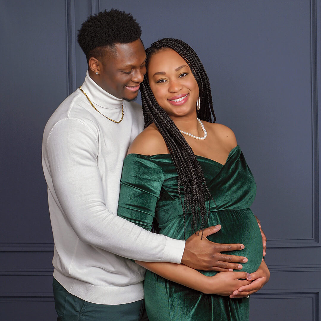 Woman in velvet dress and a man posing for maternity photos