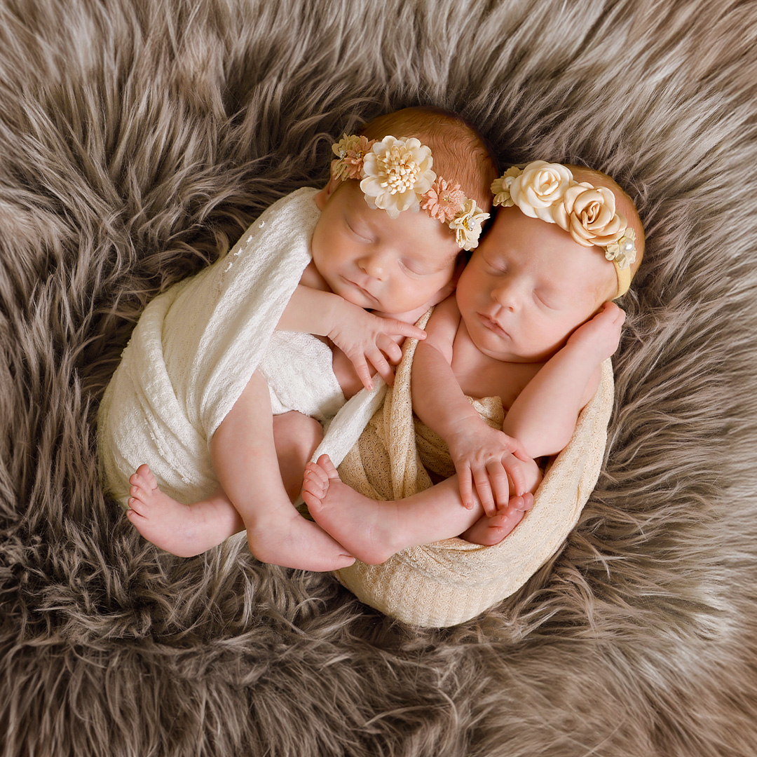 Newborn twins laying on brown fur with flower headbands