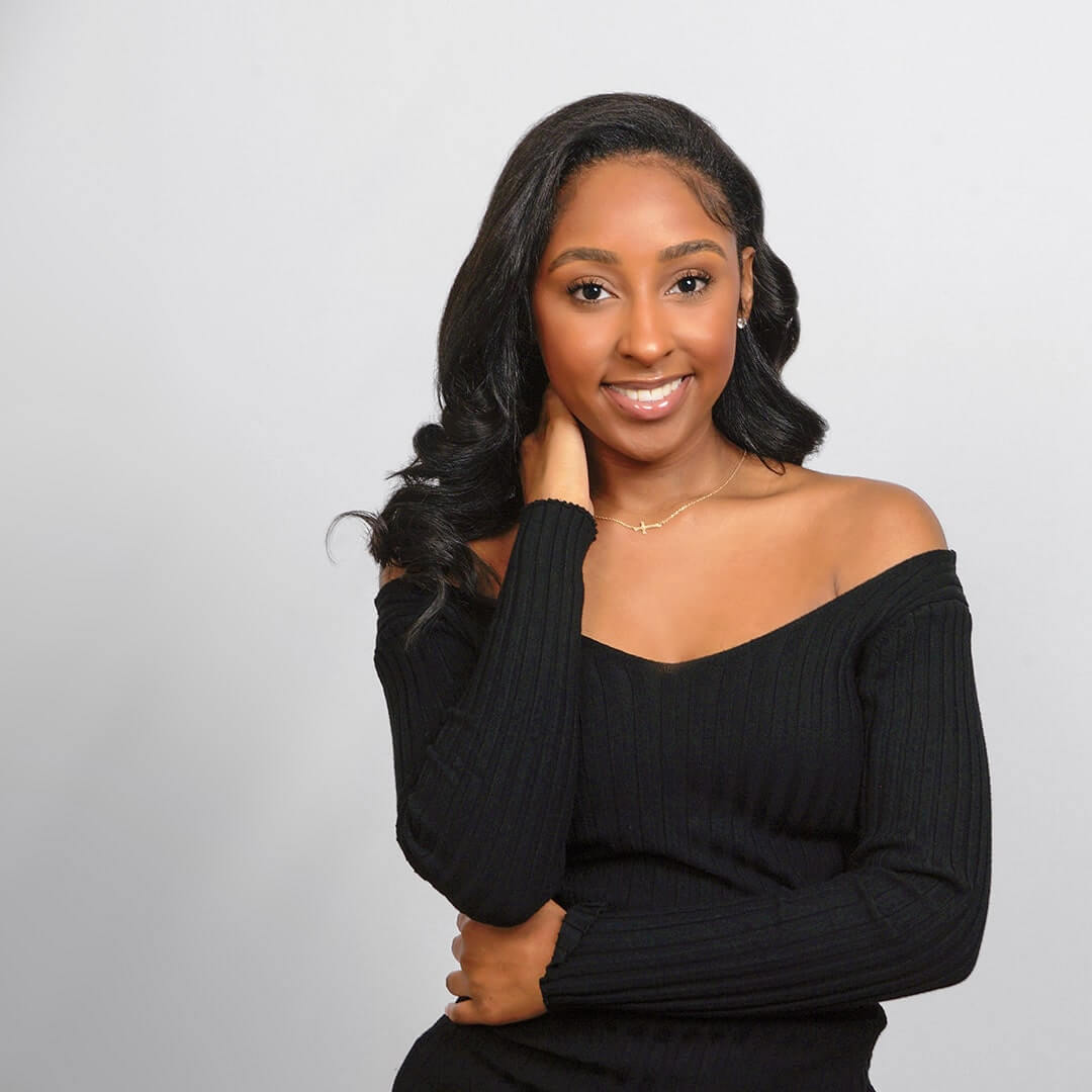 Woman in a black top posing on a white background for senior pictures.